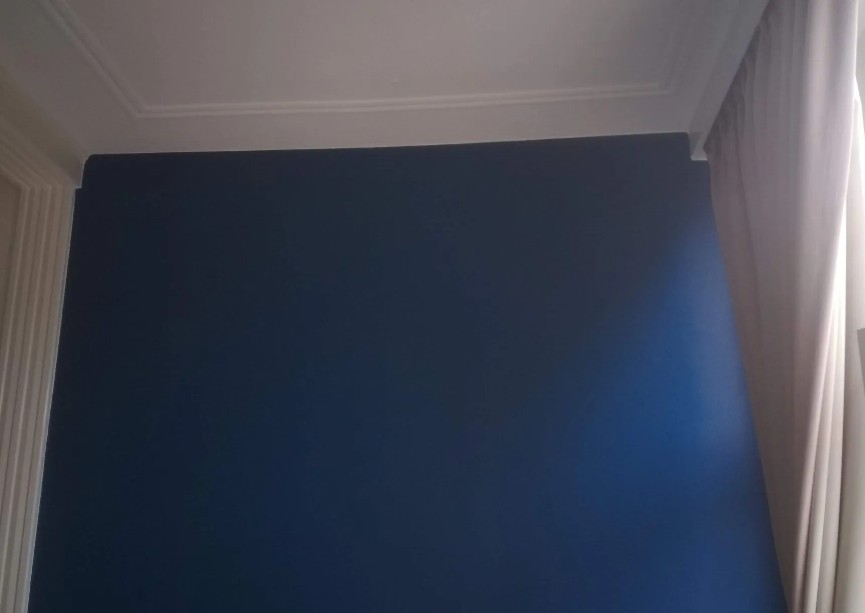 Donkerblauw geschilderde wand met strak afgezette witte plafondlijst en deurkozijn in een woonkamer