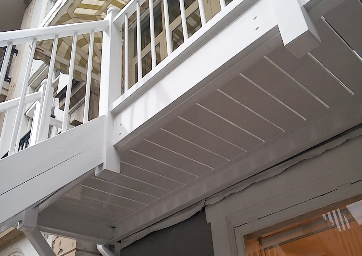 Pas geschilderde witte onderzijde van een balkon met balustrade, van onderaf gezien
