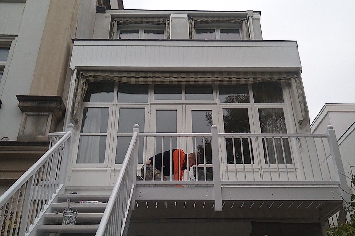 Schilder aan het werk op het balkon van een Haags herenhuis; de balustrade en de trap zijn pas wit geschilderd